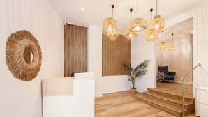 A modern reception area with a wooden reception desk, a large woven mirror, and a staircase leading to a living area. - Arenal Suites Benidorm (Benidorm)