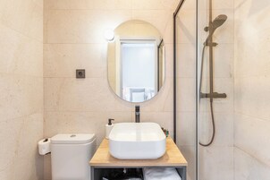 A bathroom with a white sink, a mirror, a toilet, and a shower.