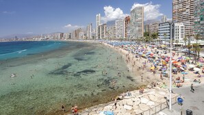 A beach with clear water, umbrellas, and people. - Arenal Suites Benidorm (Benidorm)
