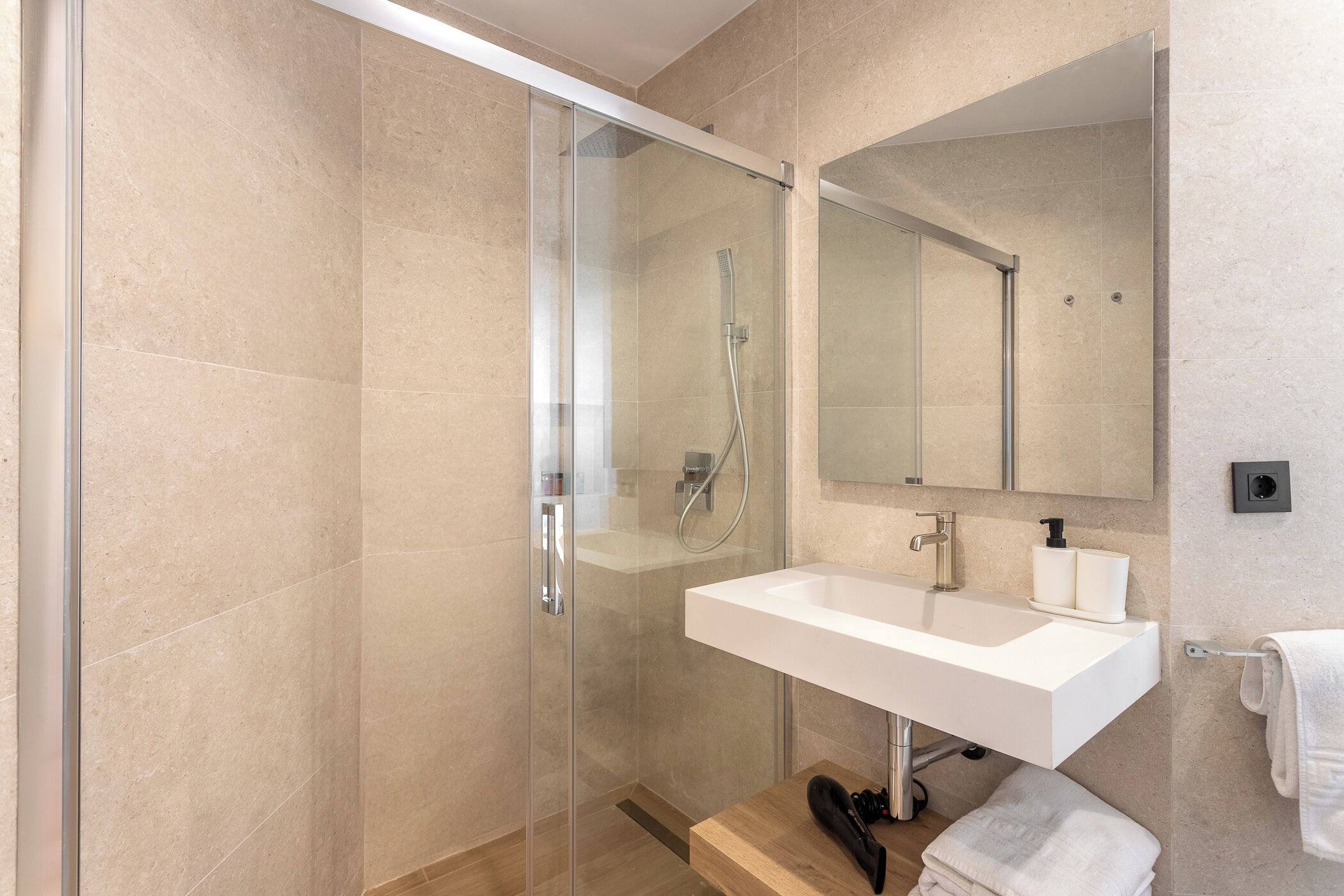Un baño moderno con ducha de vidrio, un lavamanos blanco y un espejo grande.