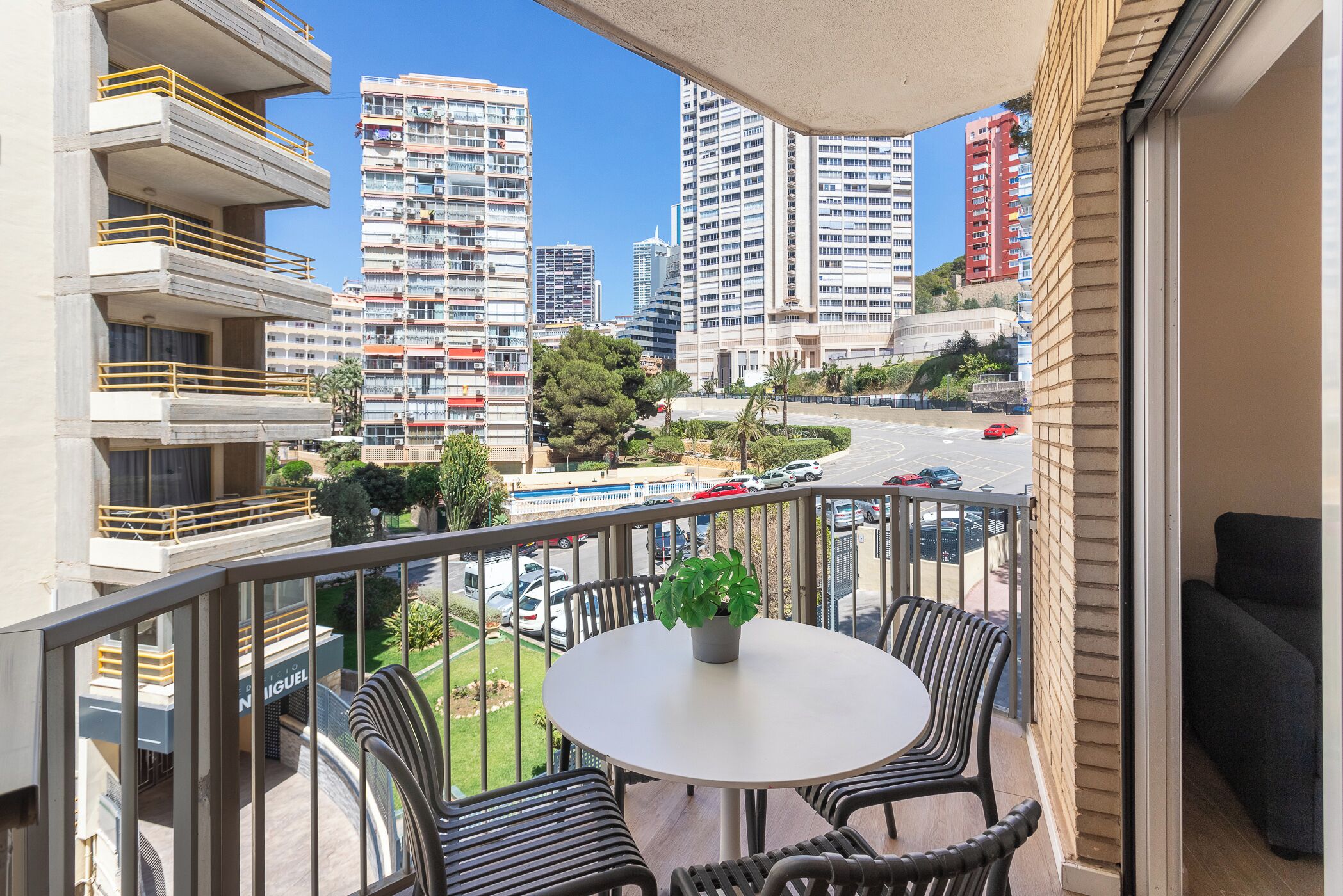 Ein Balkon mit Tisch und Stühlen, der auf einen Stadtblick mit hohen Gebäuden und einem Parkplatz blickt.