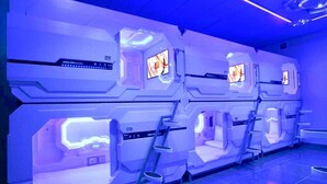 A futuristic room with four individual pods, each equipped with a control panel and a screen. - Bestow Hostel (Kuala Lumpur)