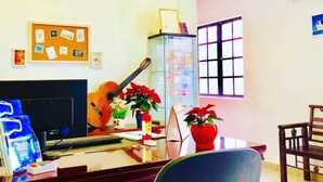 A living room with a television, a guitar, and a bulletin board on the wall. - Bestow Hostel (Kuala Lumpur)