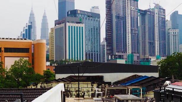 A rooftop terrace with outdoor seating, overlooking a cityscape with modern high-rise buildings. - Bestow Hostel (Kuala Lumpur)