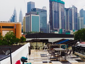 A rooftop terrace with outdoor seating, overlooking a cityscape with modern high-rise buildings. - Bestow Hostel (Kuala Lumpur)