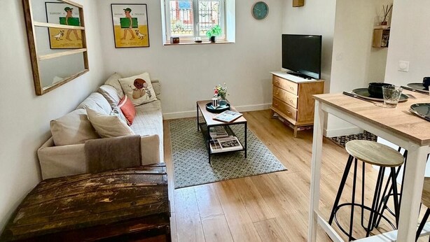 A compact living space with a sofa, coffee table, TV, and a small kitchen area. - Nid Douillet de 45 m2, Centre-ville, 2 Chambres (Trouville-sur-Mer)