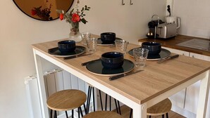 A modern kitchen with a wooden table, black stools, and a round mirror on the wall. - Nid Douillet de 45 m2, Centre-ville, 2 Chambres (Trouville-sur-Mer)