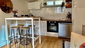 A modern kitchen with white cabinets, a central island with stools, and stainless steel appliances. - Nid Douillet de 45 m2, Centre-ville, 2 Chambres (Trouville-sur-Mer)