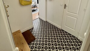 A hallway with a black and white patterned floor, a wooden bench, a yellow bag, and a white door. - Nid Douillet de 45 m2, Centre-ville, 2 Chambres (Trouville-sur-Mer)