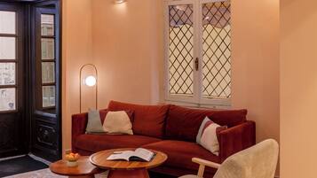 Una sala de estar acogedora con un sofá rojo, una mesa de centro de madera y un sillón beige. Hay una alfombra estampada en el suelo y una lámpara de pared decorativa.