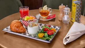 A breakfast setting with a croissant, fruit bowl, yogurt, tea, and a bottle of olive oil on a table. - Numa Rome Portico (Rome)