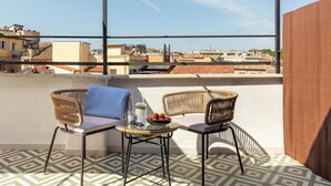 A rooftop terrace with two wicker chairs, a small table, and a bowl of fruit. The terrace has patterned floor tiles and a view of the cityscape. - Numa Rome Portico (Rome)