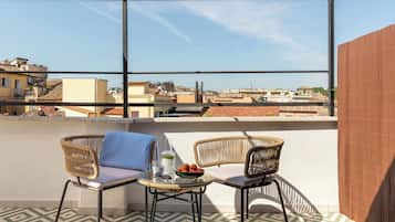 Una terraza en la azotea con dos sillas de mimbre, una mesita y un cuenco de fruta. La terraza tiene baldosas con diseños y vistas de la ciudad.