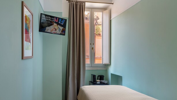 A bedroom with a bed, a window with curtains, a wall-mounted poster, and a small table with a kettle and cups. - Numa Rome Portico (Rome)
