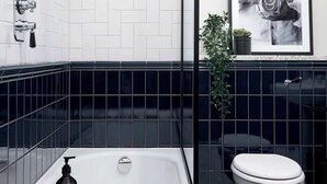 Un bagno moderno con una vasca da bagno bianca, piastrelle nere, un quadro con cornice nera e una pianta in vaso.
