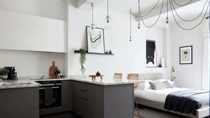 Una cucina moderna con isola centrale, zona pranzo con sedie e camera da letto con letto e comodino.