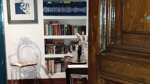 A wooden door with a brass handle, a bookshelf filled with books, a framed picture on the wall, and a clear chair.