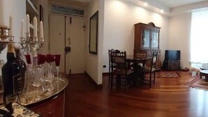 A living room with a wooden floor, a dining table with chairs, a black sofa, and a television.
