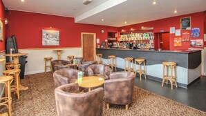Un espace bar avec des fauteuils en cuir, un comptoir et un mur rouge orné d’une horloge et de panneaux affichant le menu.