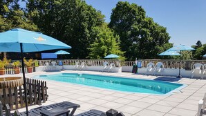 Une piscine dotée d’une terrasse carrelée, entourée de chaises longues blanches et de parasols bleus.