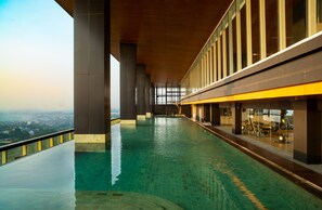 Una larga piscina interior con vistas a la ciudad, amplias ventanas y techo de madera.