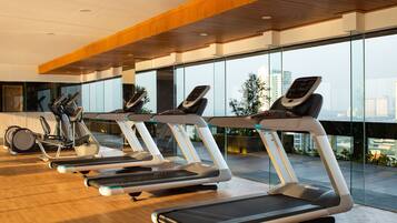 Un gimnasio con cintas de correr y elípticas, ventanas amplias y techo de madera.