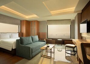 Una habitación de hotel moderna con cama, sofá, una mesita, una silla y televisor.
