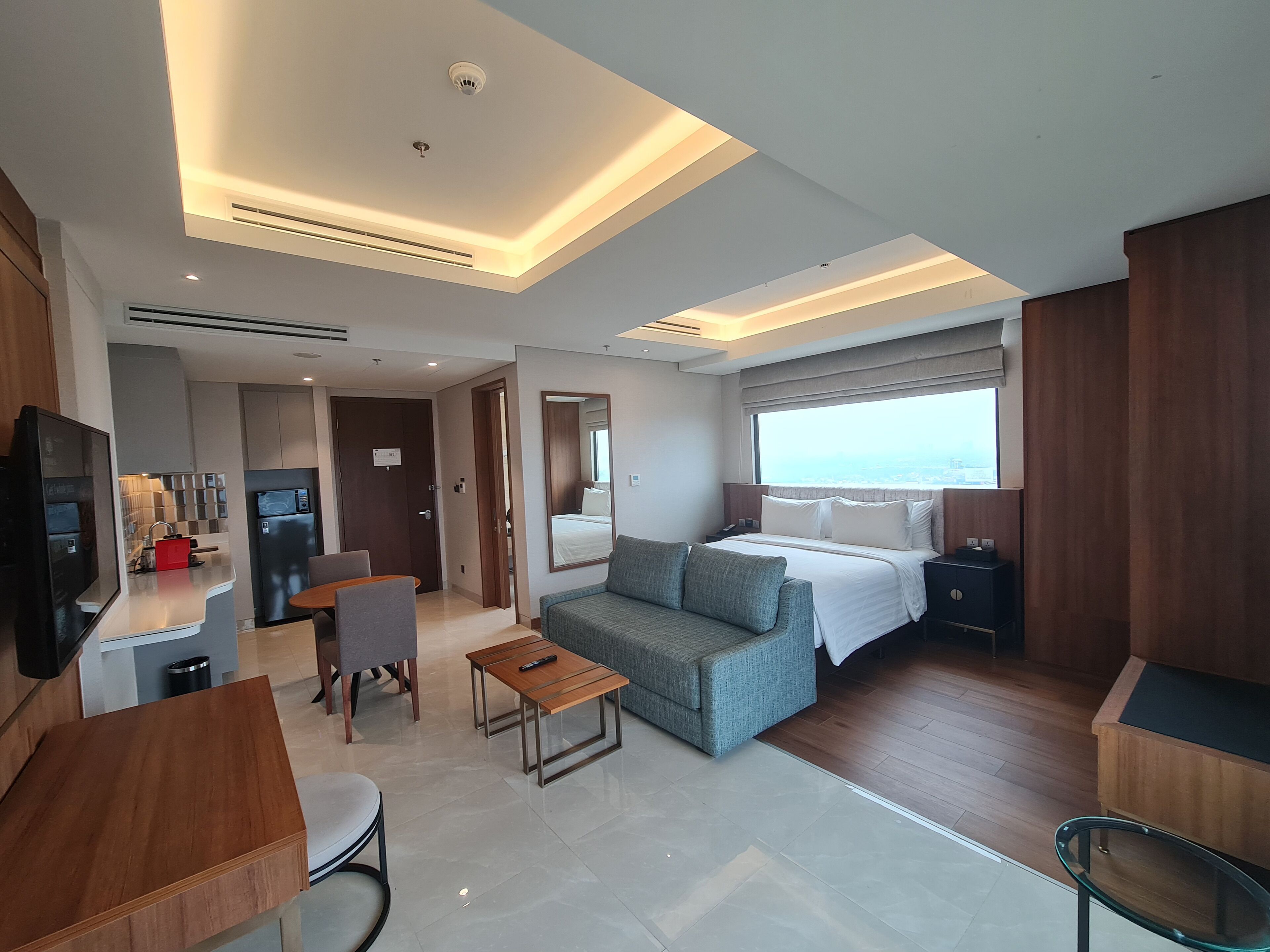 A modern hotel room with a bed, a sofa, a desk, and a TV.