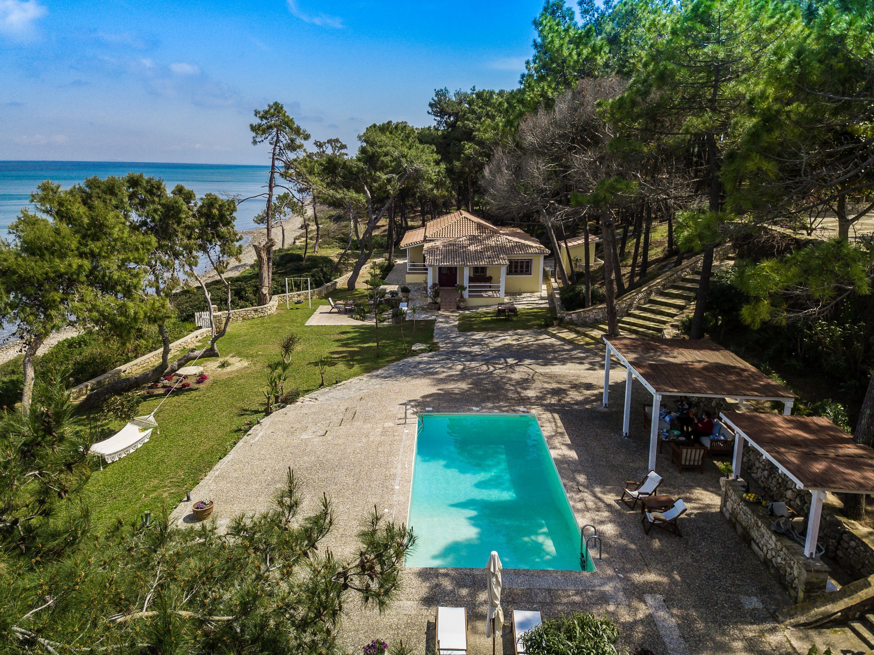 A house with a swimming pool, surrounded by trees and a view of the sea.