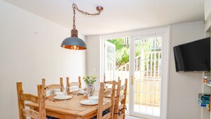 Un coin repas avec une table et des chaises en bois, un luminaire suspendu et un téléviseur fixé au mur.