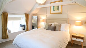 Une chambre à coucher avec un grand lit, deux tables de chevet avec des lampes, une fenêtre avec des rideaux et un luminaire au plafond.