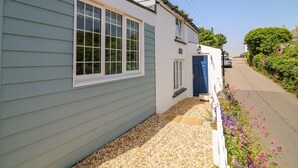 Une maison à deux étages avec une porte bleue, un petit jardin avec du gravier et des fleurs, et un ciel dégagé.
