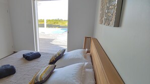 Un dormitorio con cama, almohadas, cabecero de madera y vista a una piscina al aire libre.