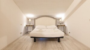 A bedroom with a bed centered under a sloped ceiling, flanked by two bedside tables with lamps.