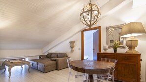 A spacious loft with a high ceiling, a dining table with chairs, a sofa, a wooden cabinet, and a chandelier.