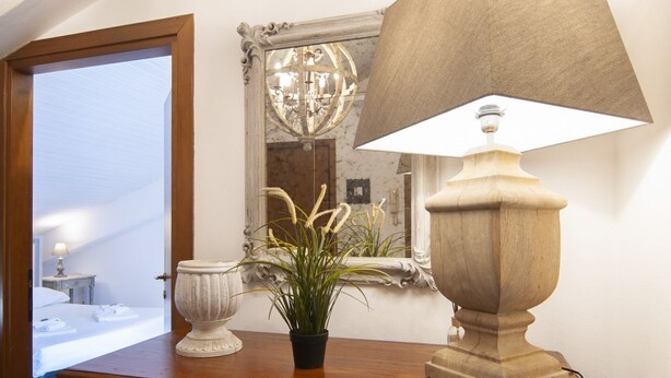 A wooden bedside table with a lamp, a potted plant, and a decorative urn.