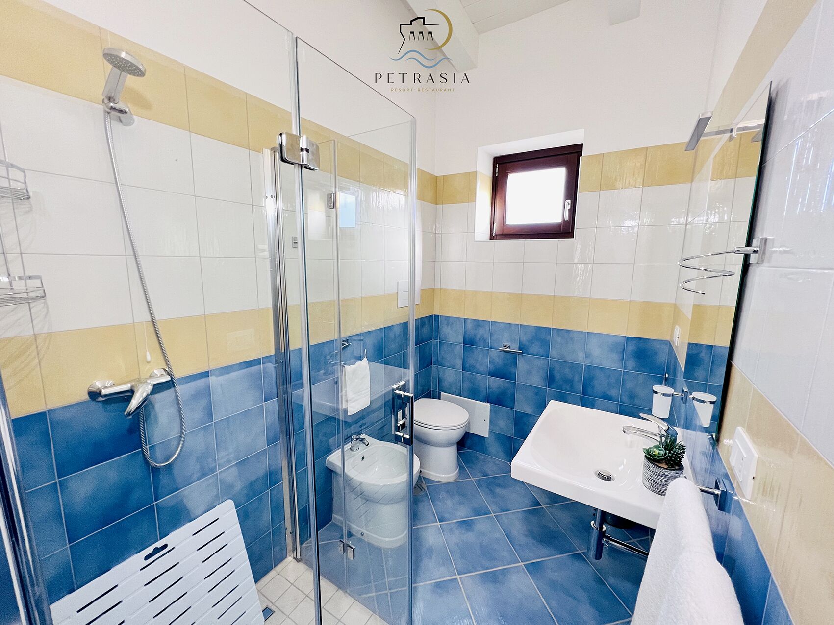 Ein Badezimmer mit einer Duschkabine, einem weißen Waschbecken, einer Toilette und einem kleinen Fenster.