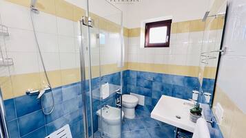 Ein Badezimmer mit einer Duschkabine, einem weißen Waschbecken, einer Toilette und einem kleinen Fenster.
