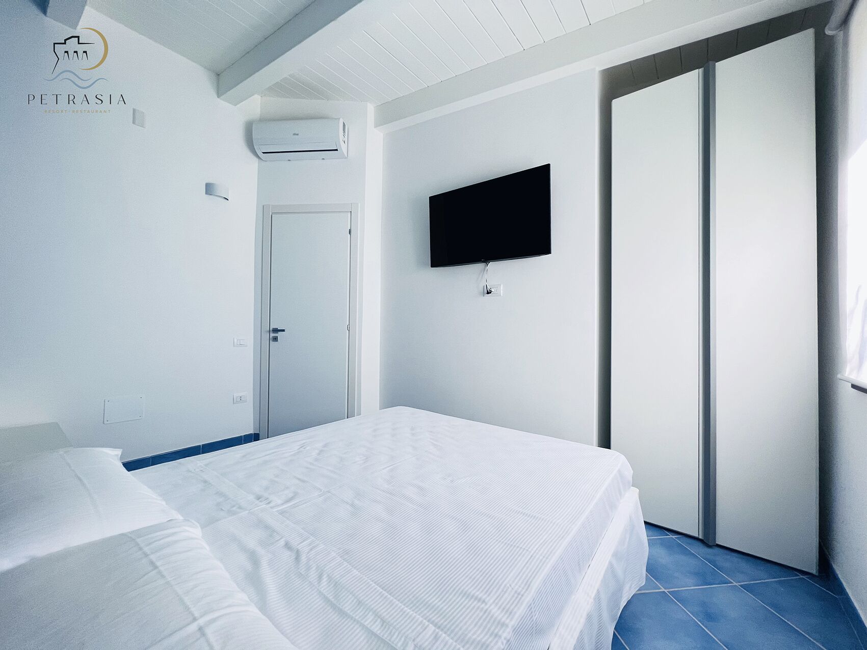 Une chambre d’hôtel avec un lit, un téléviseur fixé au mur et une porte coulissante.