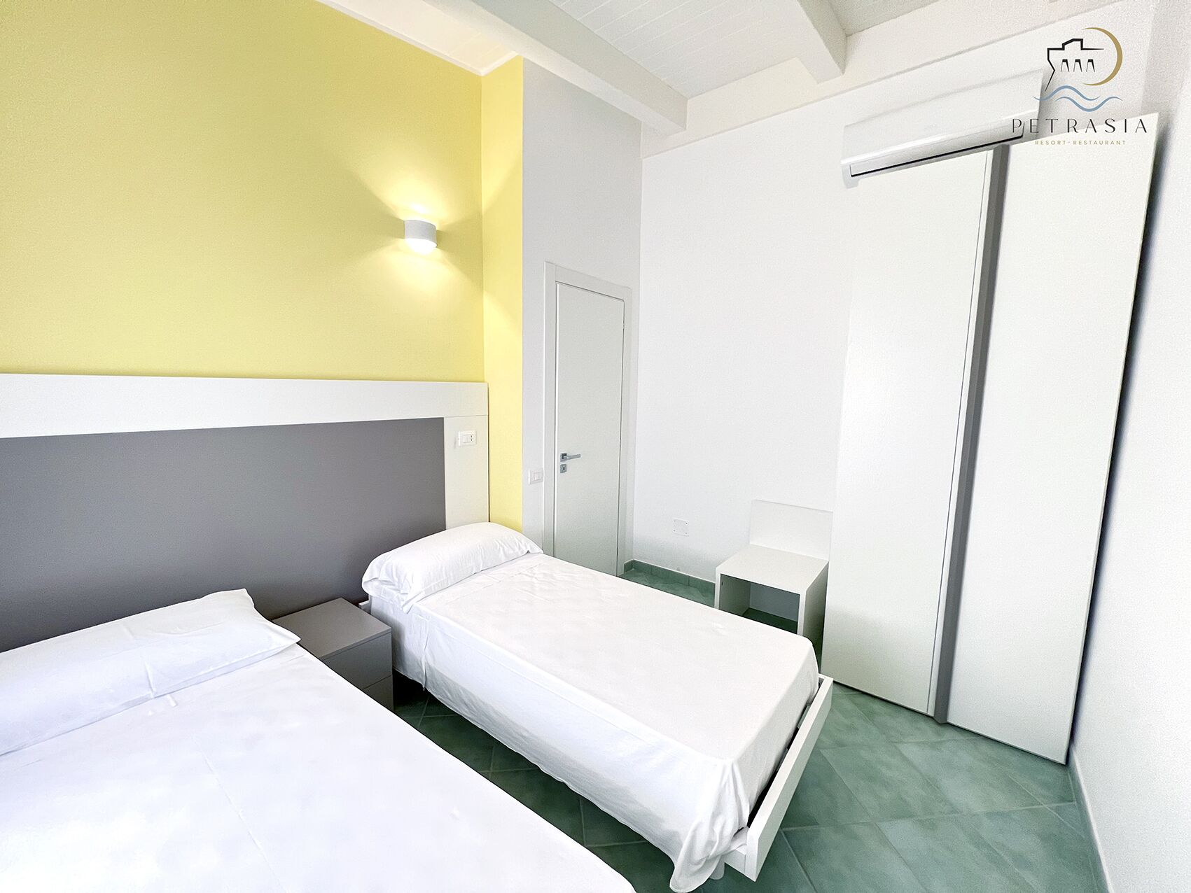 Ein Hotelzimmer mit zwei Einzelbetten, einem kleinen Nachttisch, einem Schrank und einer Wand-Klimaanlage.