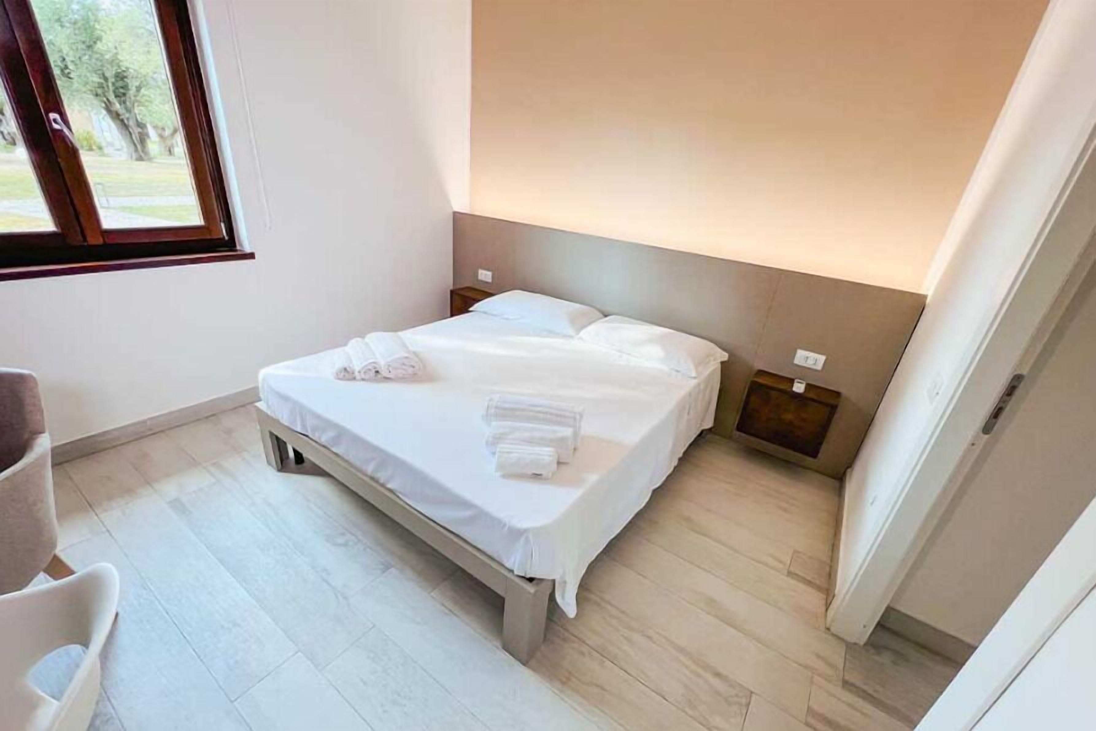 Un lit bien fait, avec du linge de lit et des serviettes blanches, une tête de lit en bois et une petite table de chevet avec une lampe.