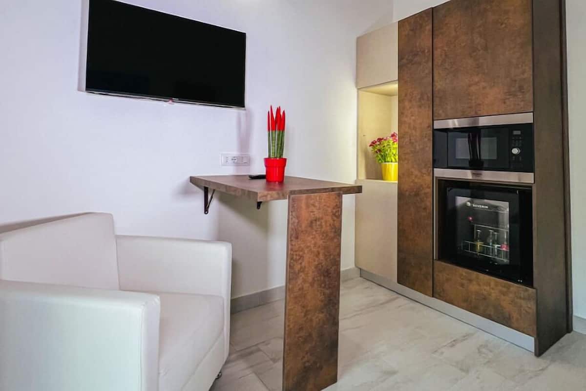 A compact kitchen with a built-in microwave and oven, a small table with a red pot, and a white couch.