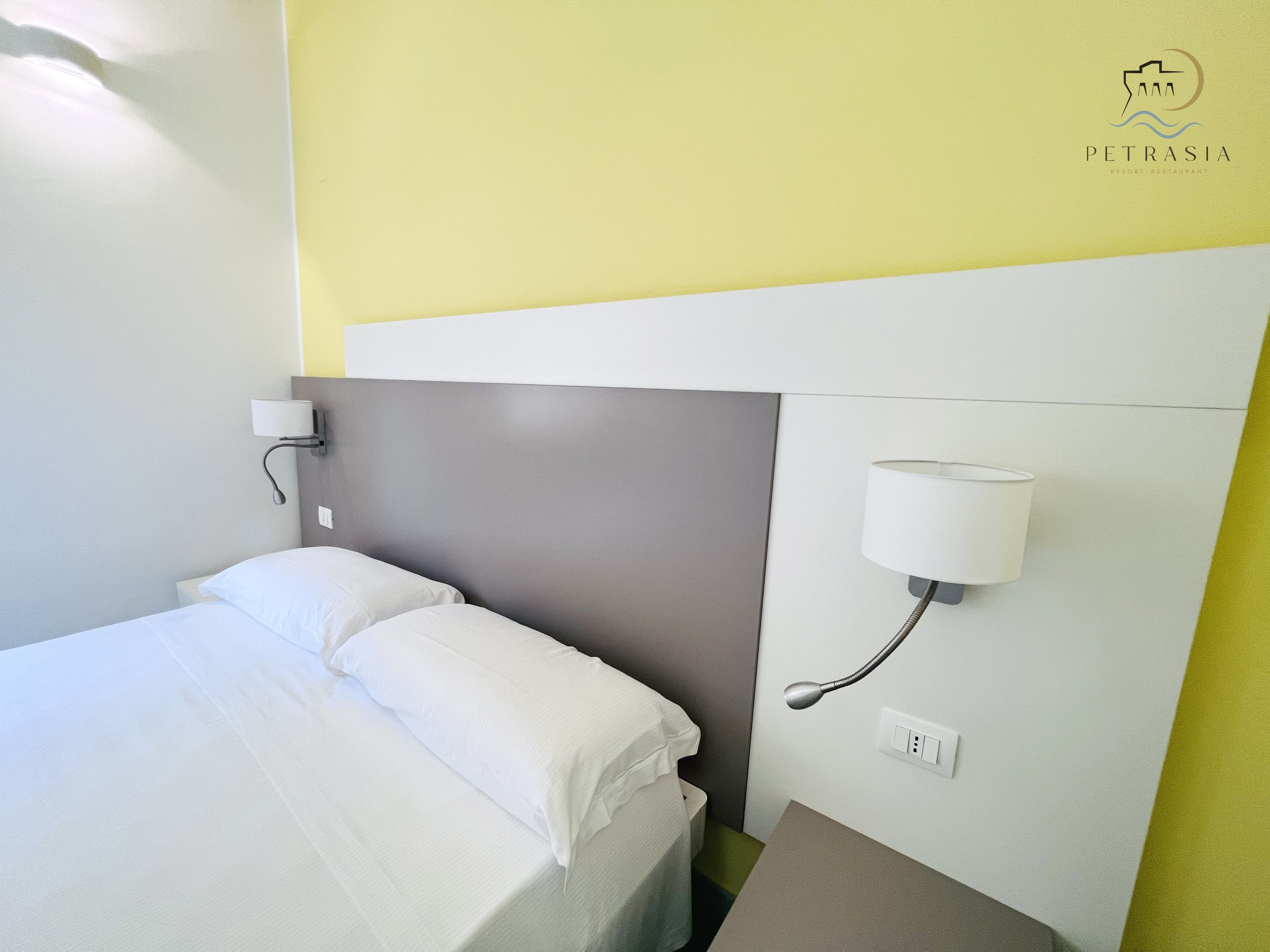 Una habitación de hotel con una cama, una mesita de noche, una lámpara de pared y un enchufe.