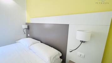 Una habitación de hotel con una cama, una mesita de noche, una lámpara de pared y un enchufe.