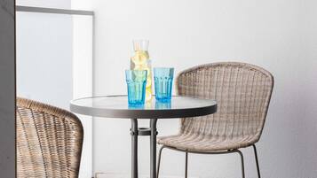 A round table with two blue glasses and a glass bottle with a straw, accompanied by wicker chairs.