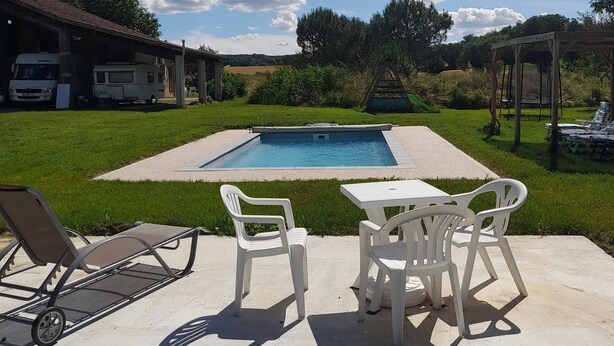 A backyard with a swimming pool, outdoor seating, and a covered area.