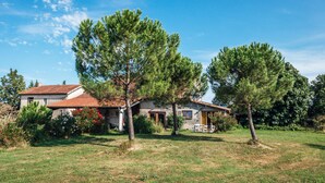 A house with a red-tiled roof, surrounded by a grassy lawn and trees.