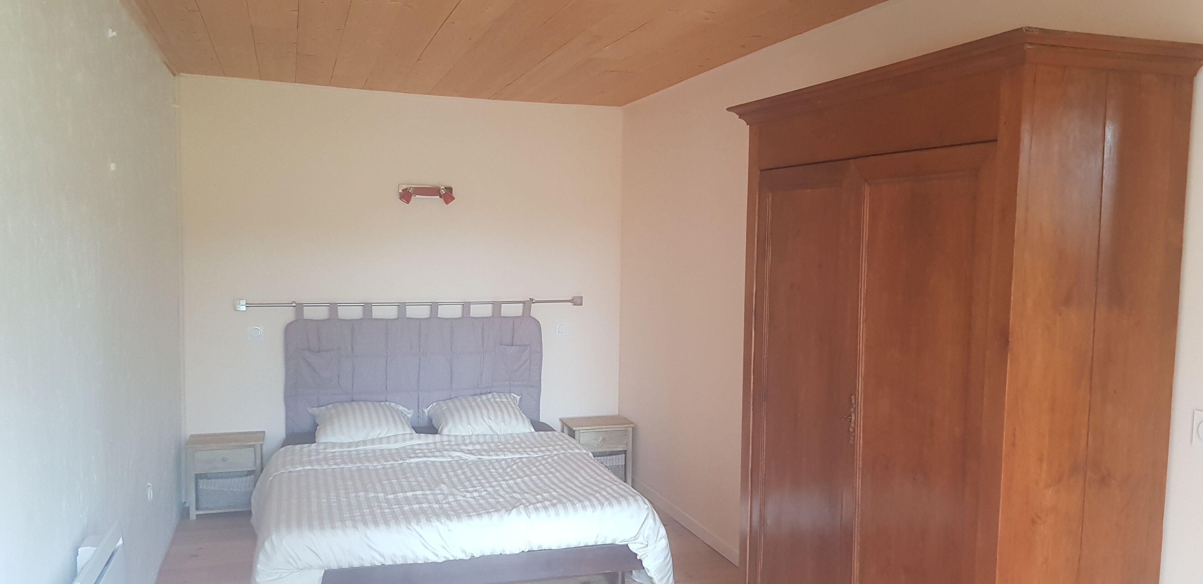 Une chambre à coucher comprenant un lit, une armoire en bois, des tables de chevet et un luminaire fixé au plafond.