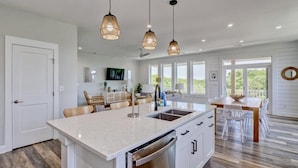 A modern kitchen with a large island, pendant lighting, and a dining area with a wooden table and chairs.