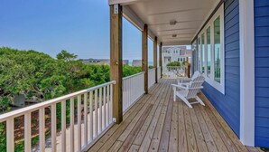 A wooden deck with white railings, a covered area, and a view of the ocean.